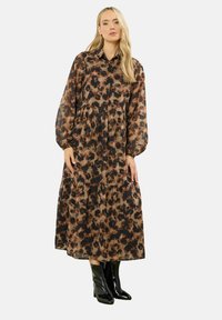 Brązowa i czarna maxi sukienka w wzory z długimi rękawami, z guzikowym kołnierzykiem i warstwowym dołem. Połączona z błyszczącymi czarnymi botkami za kostkę.