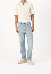 Camisa de manga corta de color beige claro con cuello, combinada con unos pantalones vaqueros rectos de color azul claro y zapatillas de color crema. Textura de tela lisa.