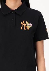 Black polo shirt made of cotton. Features an orange embroidered "NY" logo with floral accents. Includes a classic collar and short sleeves.