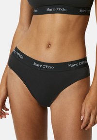 Zwarte katoenen bikini slip met een brede elastische tailleband waarop het "Marc O'Polo"-logo in het wit staat afgebeeld. Gladde textuur en een aangesloten pasvorm.