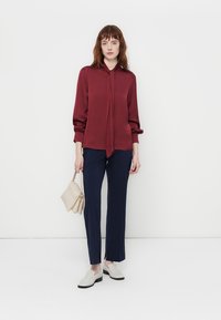 Burgundijas zīda blūze ar saišu detaļu, apvienota ar tumši zila rūtainām biksēm, gaiši beidžu somu un baltām slip-on kurpēm. Minimalistisks dizains.