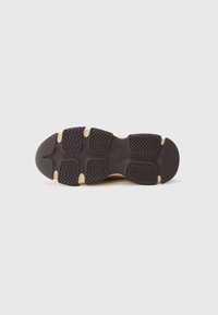 Suela de goma negra con un patrón de tracción texturado, que presenta surcos pronunciados y acentos beige en los bordes. Diseño plano para mayor estabilidad.