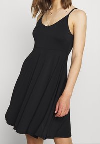 Abito nero senza maniche con scollo a V, corpetto aderente e gonna svasata. Realizzato in un tessuto liscio e leggero con un design classico.