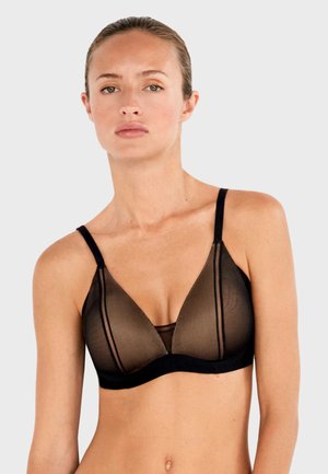 Kobieta nosząca czarny prześwitujący siateczkowy bralet z cienkimi ramiączkami, pozująca na tle jednolitego jasnoszarego tła.