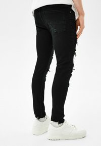 Smal svarta denimjeans med slitna detaljer längs sömmarna, fransade fållar och två bakfickor. Bärs med vita sneakers.