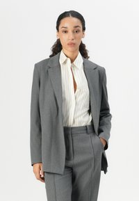 Gray pinstriped suit with a wide, tailored blazer and matching trousers. Underneath, a light-colored striped shirt. Smooth fabric texture.