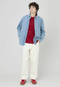 Chemise en denim bleu clair sur un T-shirt rouge, associée à un pantalon ample blanc et des sneakers rouges avec des rayures blanches.
