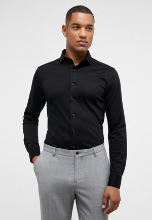Schwarz langärmliges Hemd mit Button-Down-Kragen, verfügt über eine glatte Textur und eine taillierte Passform, kombiniert mit hellgrauen Hosen.