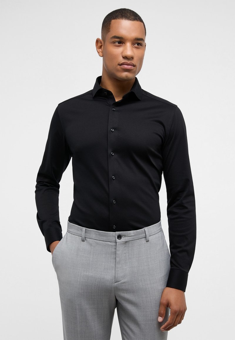 Zwarte long sleeve shirt met een button-down kraag, met een gladde textuur en een getailleerd ontwerp, gecombineerd met lichtgrijze broek.