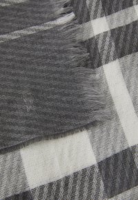 Woven blanket featuring a gray and white checkered pattern. The edges have frayed detailing, with a soft cotton texture.