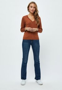 Brauner V-Ausschnitt-Pullover kombiniert mit blauen Jeans und weißen Sneakers. Lange Ärmel, taillierte Passform und strukturierte Strickoberfläche.