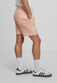 Perzikkleurige shorts van textuurstof met zijzakken, een elastische tailleband en een enkele achterzak. Gemaakt met witte sokken en sneakers.