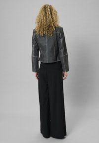 Gray leather jacket with contrasting stitching, cropped design, and long black wide-leg trousers, viewed from the back.