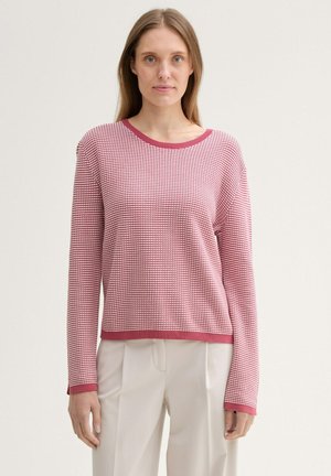 Textured sweater in red and pink, round neckline, long sleeves, ribbed hem and cuffs, boxy fit. Worn with beige trousers.