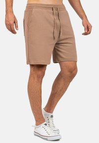 Shorts in cotone marrone misto con vita elastica e cordoncino, tasche laterali e vestibilità rilassata, abbinati a sneaker bianche.