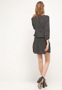 Černé šaty s vzorem v diamantech, krátká sukně, dlouhé rukávy a nařasený pas. Spárovány s černými sandály na robustním podpatku.