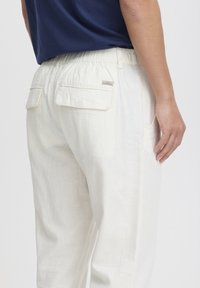 Witte linnen broek met een relaxed fit, elastische tailleband en twee achterzakken. Kenmerkt zich door een klein merklabel nabij de tailleband.