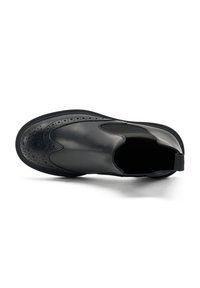 Scarpa slip-on in pelle nera con design brogue, dettagli perforati, pannelli laterali elasticizzati e suola in gomma nera resistente.