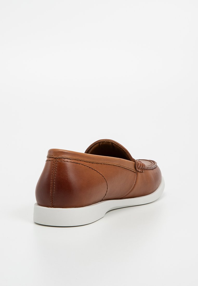 Chaussure en cuir marron avec une texture lisse, de forme arrondie et une semelle en caoutchouc blanche. Présente des détails de couture et un design à enfiler.