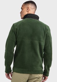 Grüne Fleecejacke mit schwarzem Kragen, die eine weiche Textur und eine lockere Passform aufweist. Bemerkenswert für ihre Schlichtheit und das Fehlen sichtbarer Beschläge.