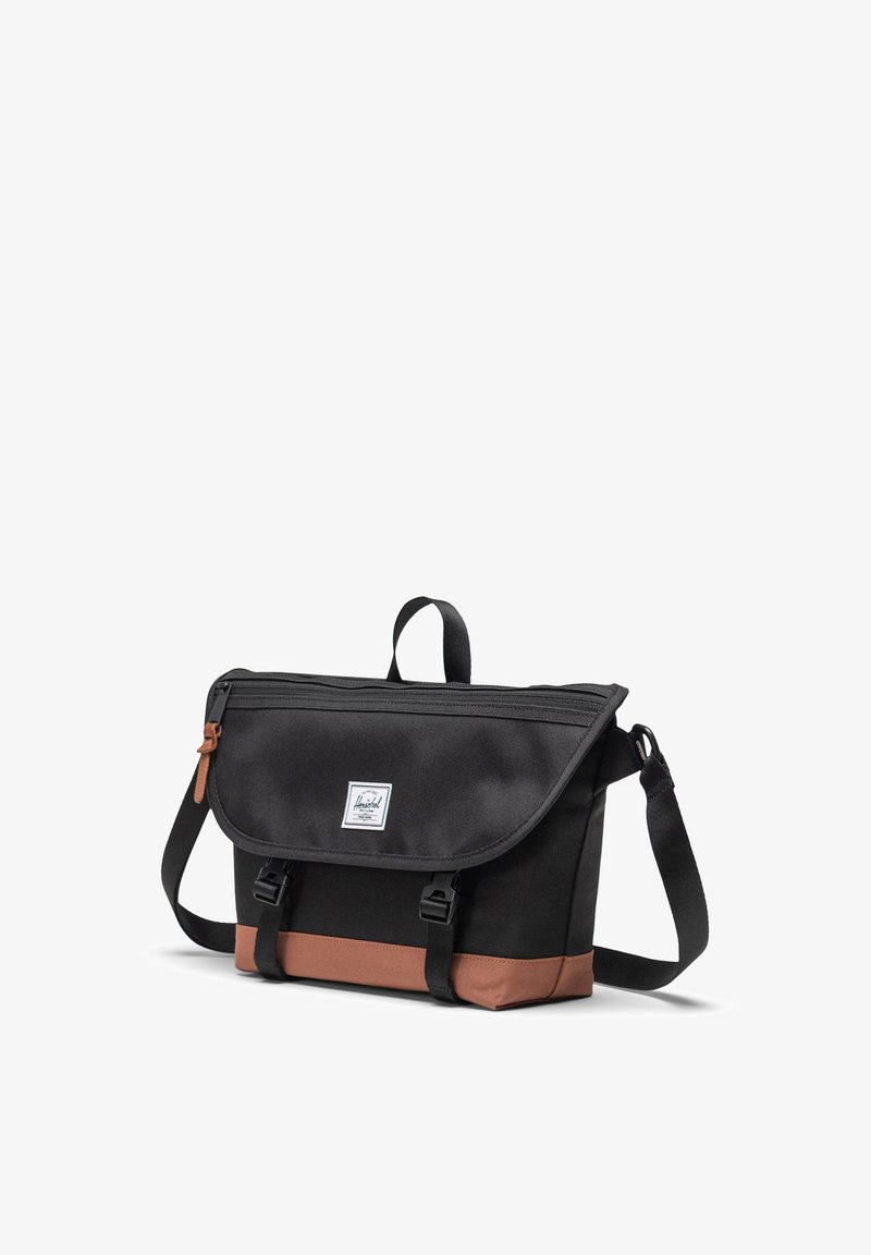 Sort canvas messenger bag med en brun nedre panel, fold-over klap, justerbar rem og lynlås lukning. Funktionen har et logo patch på forsiden.