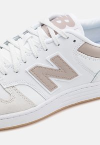 Baltas sneakers ar teksturētu zamšu un gludu ādu. Iekļauj beigu ādas 'N' logotipu, baltas šņores un gumijas zolīti.