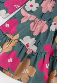 Blumenkleid aus weicher Baumwolle mit einem türkisfarbenen Hintergrund und rosa, weißen und pfirsichfarbenen Blumen. Es hat Rüschenschichten und lange Ärmel.