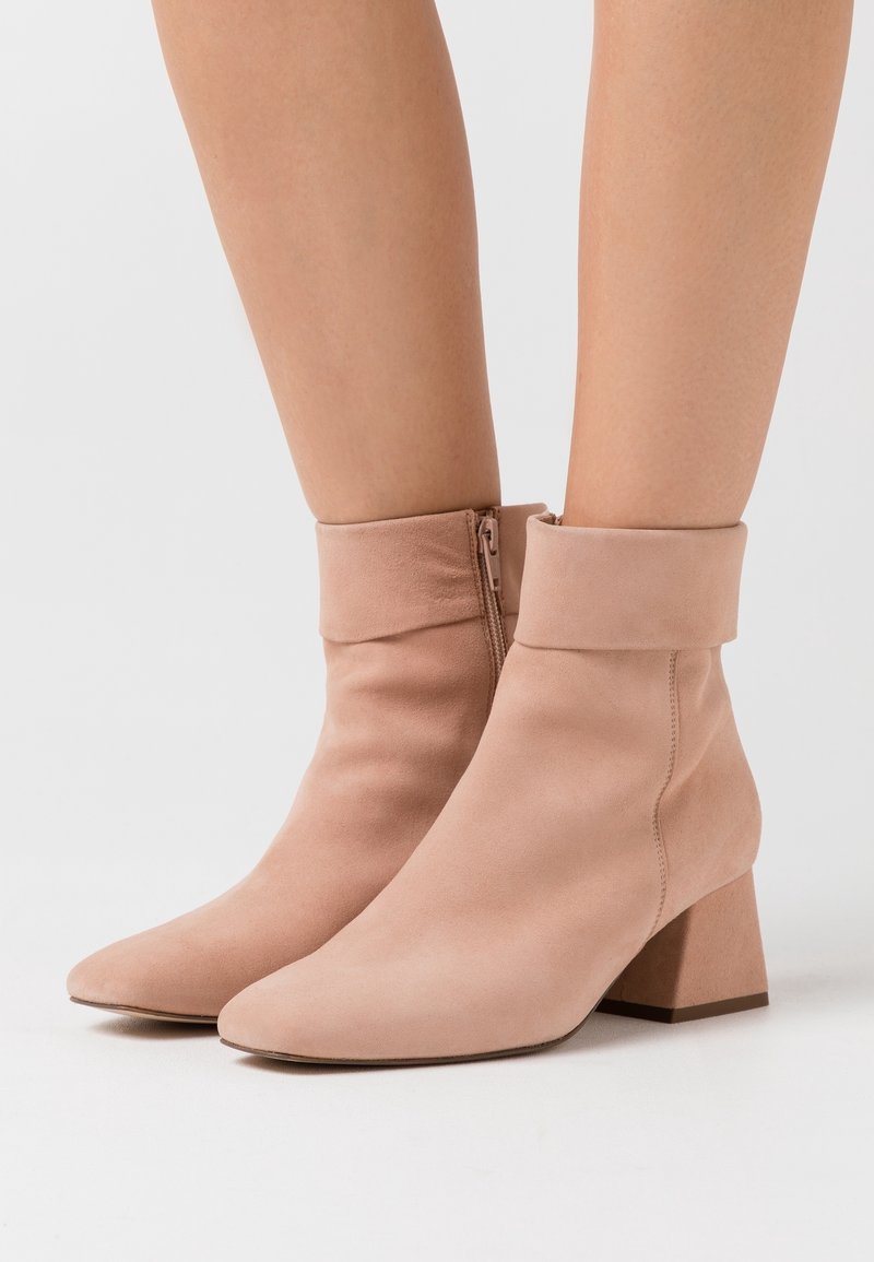 Bottes cheville en daim rose avec un bout pointu, un talon épais et un design à revers plié. Dotées d'une fermeture éclair latérale pour un enfilage facile.