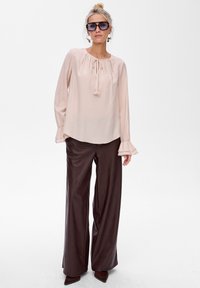 Jasnoróżowa bluzka z długim rękawem, z gromadzonym dekoltem i wiązaniem, zestawiona z ciemnobrązowymi spodniami szerokimi i szpilkami z wąskim noskiem.