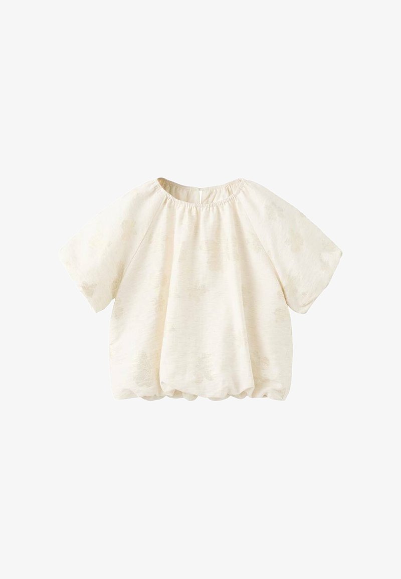 Blouse ample à manches courtes, de couleur crème, avec un col rond et un motif texturé subtil sur un tissu léger.