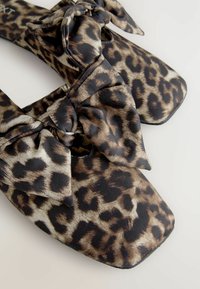 Čevlji z leopardjim vzorcem s kvadratnimi prsti, opremljeni z vidno pentljo. Narejeni iz mehkega blaga z gladko teksturo in temnimi akcenti.