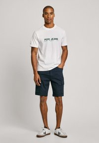 Biela bavlnená tričko s zeleným logom "PEPE JEANS", skombinované s námorníckymi cargo šortkami a bielymi teniskami s čiernymi akcentmi.