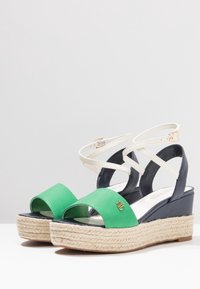 Gröna och marinblå kilklackar med en juteplattform, remmar runt ankeln och ett öppet tådäck med en detalj i guld.