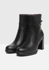 Bottines en cuir noir avec une texture lisse, dotées d'un talon carré, d'accents de boucle minimalistes et d'une fermeture éclair sur le côté.