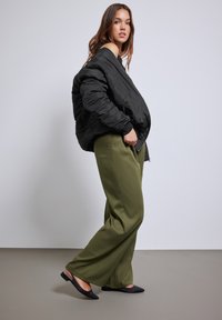 Zwarte pufferjack, oversized pasvorm, geribde manchetten. Olijfgroene wijde broek, zachte textuur, gecombineerd met zwarte puntige flats.