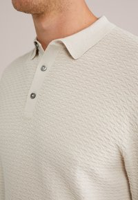 Beigā adīta polo krekls ar teksturētu dimanta rakstu, pogu platu ar divām tumšām pogām un mīkstu ribotu apkakli.