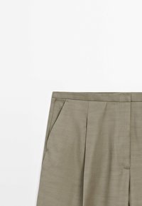 Pantalon sur mesure de couleur fauve avec poches latérales et ceinture plate sur fond blanc.