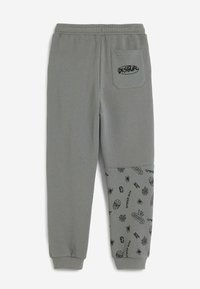 Graue Jogginghose mit einem gerippten Bund und Bündchen. Verfügt über eine aufgesetzte Tasche und bedruckte Spinnenmotive am unteren Bein. Aus Baumwollmaterial.