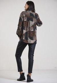 Long-sleeve shirt with abstract brown, black, and white patterns; paired with fitted black leather pants and ankle boots.