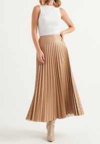 Tan plisserad midi kjol i satin. Har horisontella veck, lätt material och en slät yta. Matchad med en vit ribbad linne.