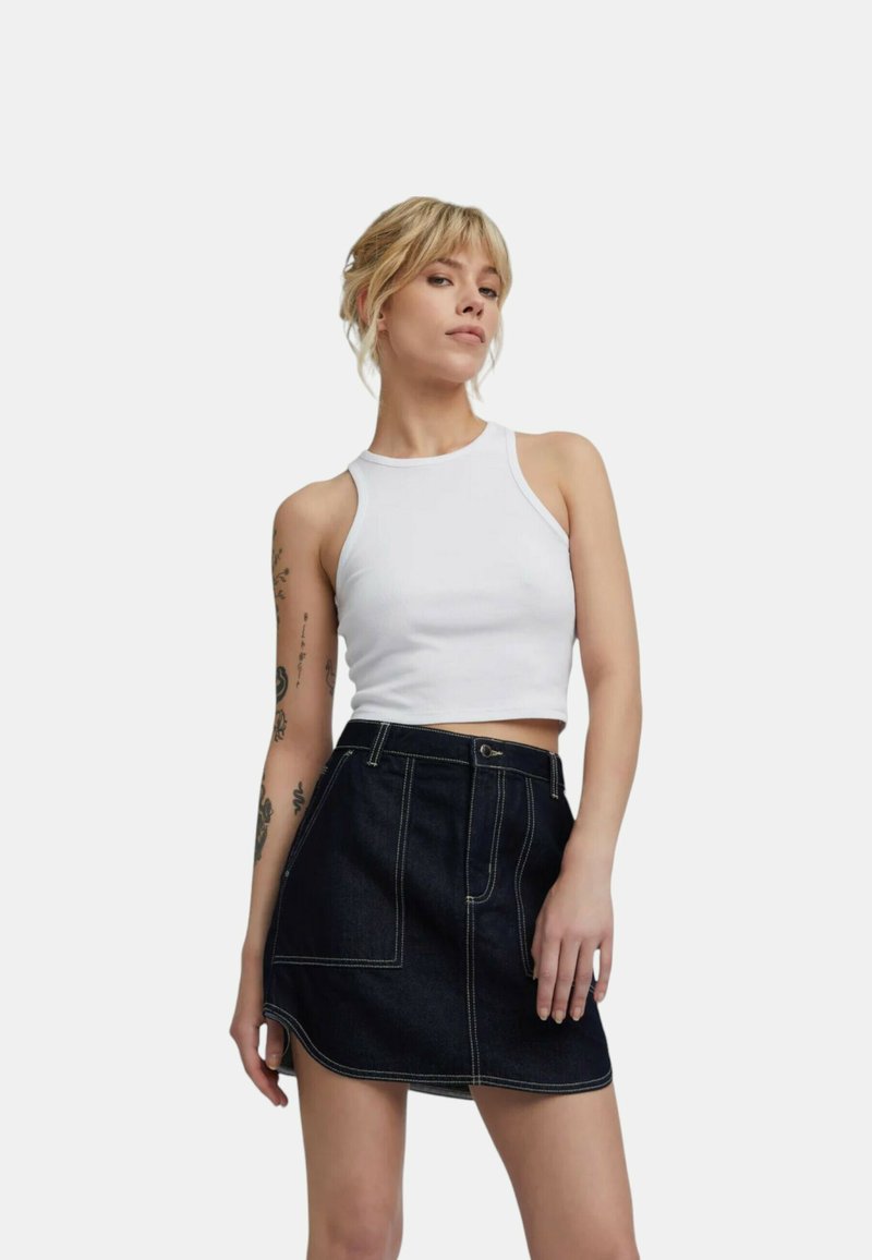 Top corto bianco a costine con scollatura rotonda abbinato a una gonna mini in denim blu scuro con cuciture bianche e una tasca laterale.