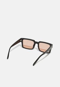 Ochelari de soare dreptunghiulari negri cu lentile roz, având o ramă groasă și brațe elegante. Design minimalist fără logo-uri sau embellishments vizibile.