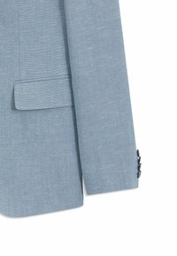 Manche d'un blazer bleu clair avec trois boutons foncés sur le poignet et une poche à rabat sur le côté, sur fond blanc.