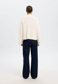 Suéter corto color crema con un acabado suave y texturizado, combinado con vaqueros de pierna ancha en azul oscuro. El conjunto presenta un ajuste relajado.