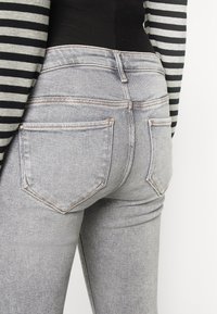 Jeans de denim gris con cintura alta, que cuentan con un diseño de cinco bolsillos y costuras en contraste. La textura es suave y con un ligero estiramiento.