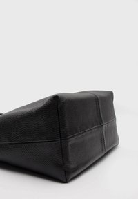 Czarna skórzana torba o teksturowanej powierzchni, prostokątnym kształcie i kanciastych rogach. Posiada widoczne przeszycia oraz usztywnione dno.