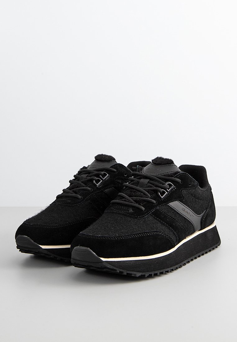 Zapatillas negras de ante y textil con un acabado texturizado, que cuentan con cordones, una suela de goma y una franja blanca contrastante en la suela exterior.