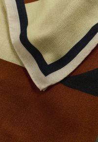 Écharpe abstraite multicolore présentant des motifs marron, crème et bleu marine. Tissu doux et texturé avec un bord ourlé.