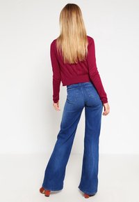 Maroon cropped sweater and flared blue jeans. Soft fabric, fitted waist, and wide legs. Smooth texture with back pockets on jeans.