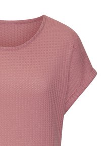 Vaaleanpunainen teksturoitu kangastoppi lyhyillä hihoilla ja pyöreällä kaula-aukolla, jossa on hienovarainen vohvelikuosi.